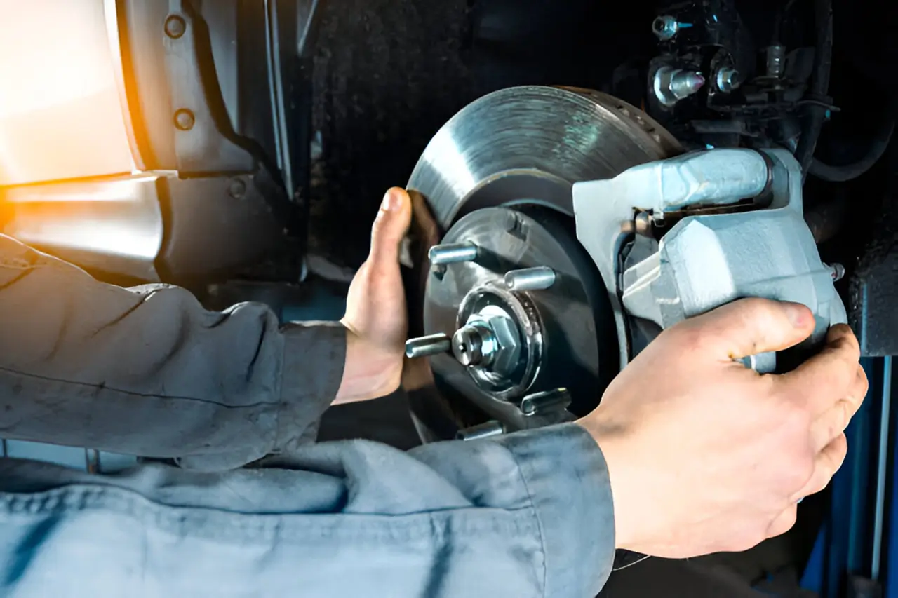 A mechanic working on a car's braking system, holding a brake caliper and rotor while performing maintenance or repairs.