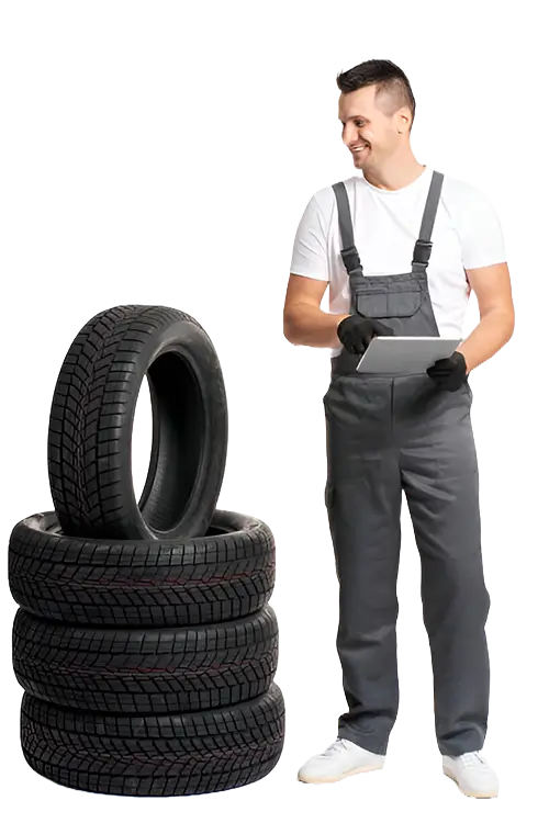 Smiling auto technician in gray overalls holding a tablet next to a stack of four car tires.
