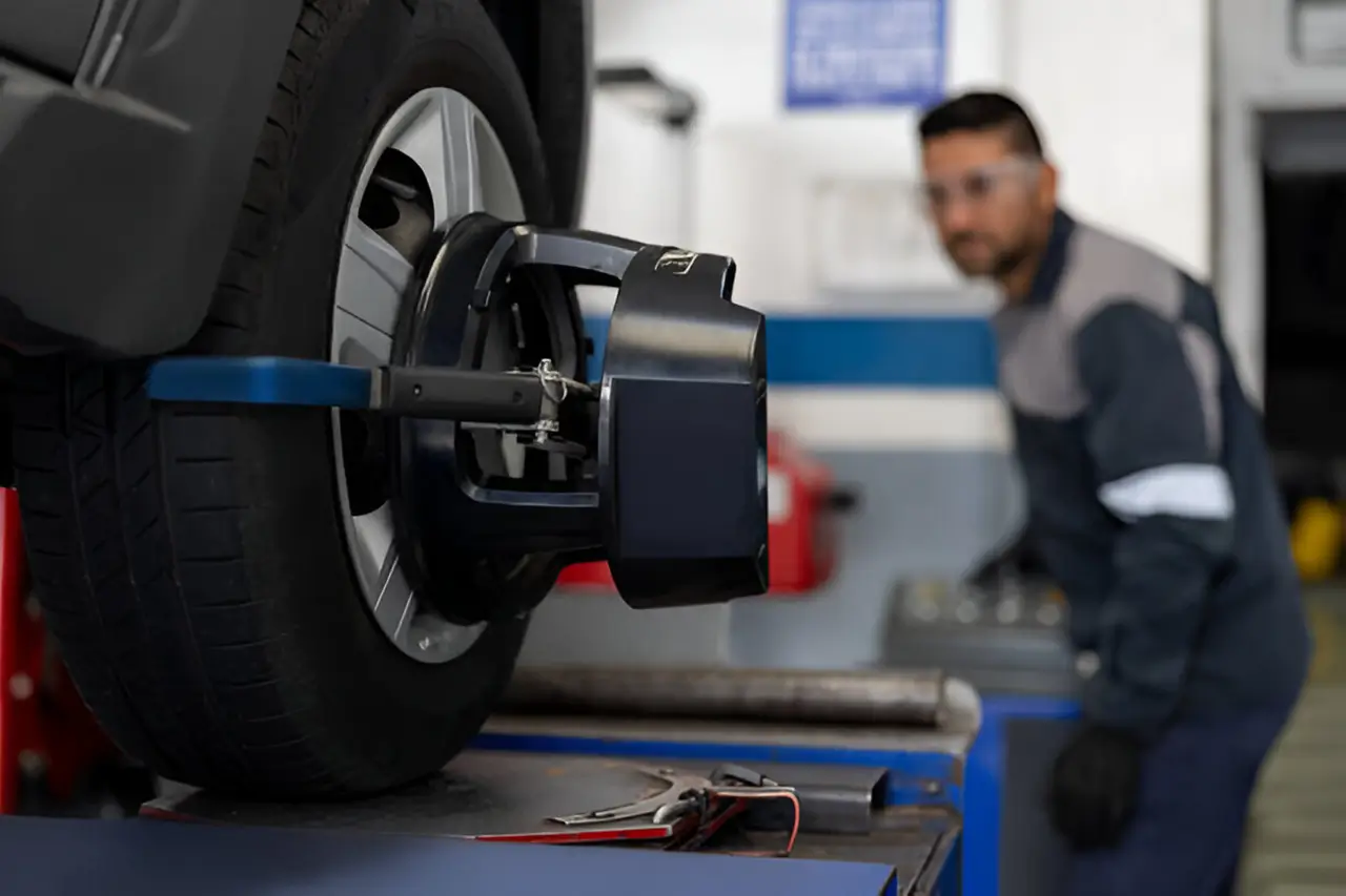 Mechanic adjusting a car wheel with precision tools in a well-lit auto repair shop.