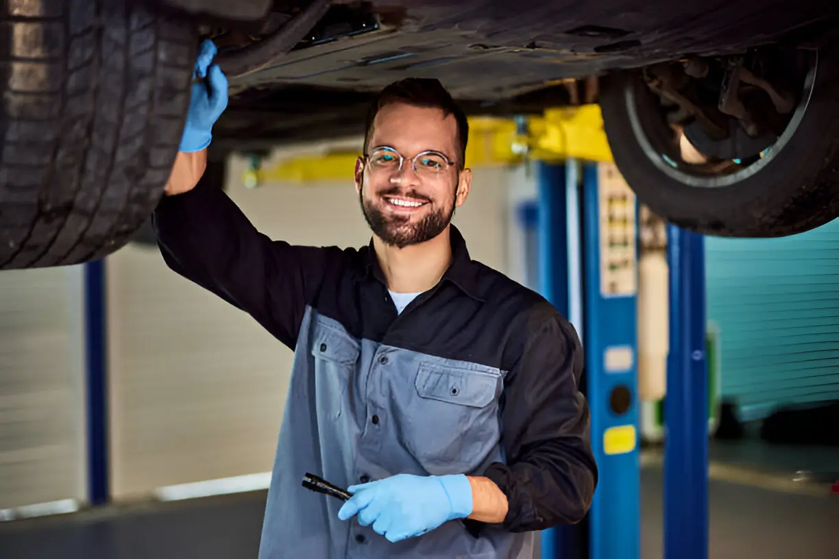 Smiling auto mechanic wearing gloves inspecting a car at a repair shop in Hamilton, ON