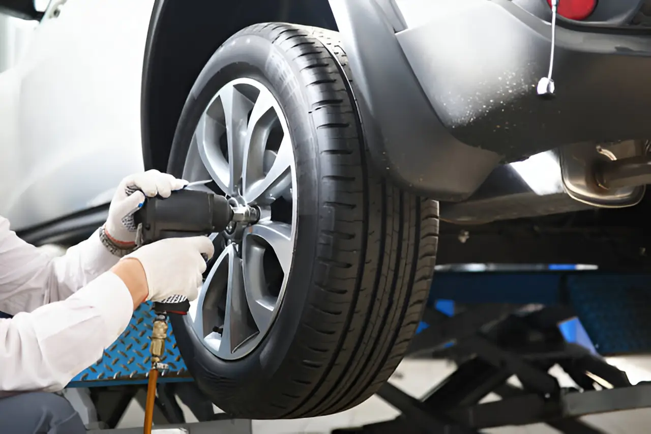 Mechanic using an impact wrench to install or remove a wheel on a raised vehicle in an auto repair shop.