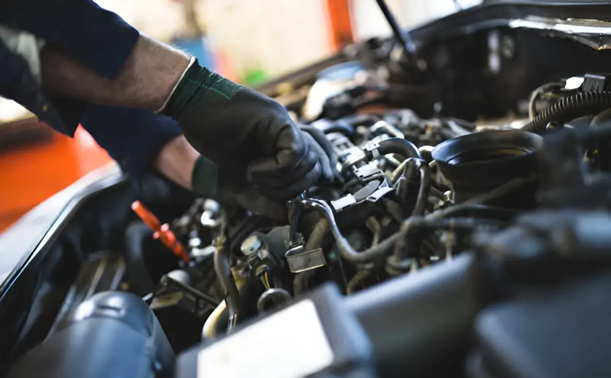 Close-up of an auto mechanic's gloved hands working on a car engine in a repair shop.