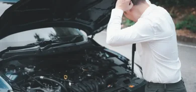 A businessman has a car breakdown – a young man stressed out by car trouble, looking at the engine failure with frustration in the morning.